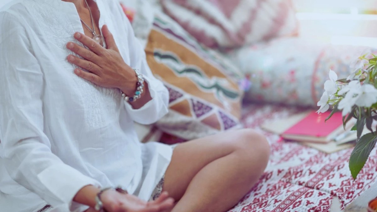 A person sitting quietly with a hand resting on their chest, in soft daylight